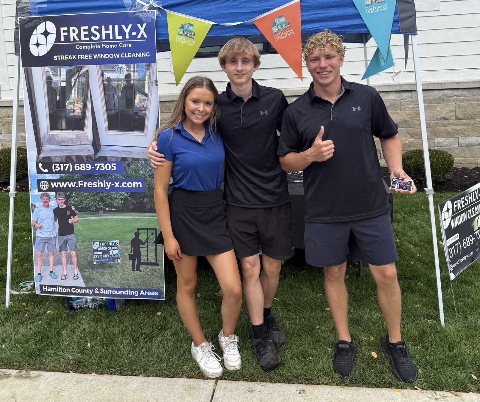 Three members of the Freshlyx team, including both co-owners, standing under a branded Freshlyx tent at a community event